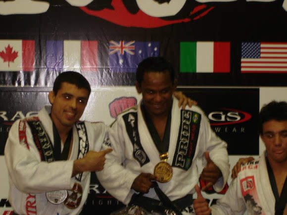 Fredson Paixão in 2005, smiling with a gold medal around his neck among other medalists, in front of a wall of national flags