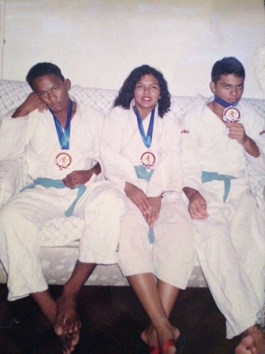 A young Fredson Paixão, far left, in a white gi and blue belt with a medal around his neck, seated beside two teammates who wear theirs