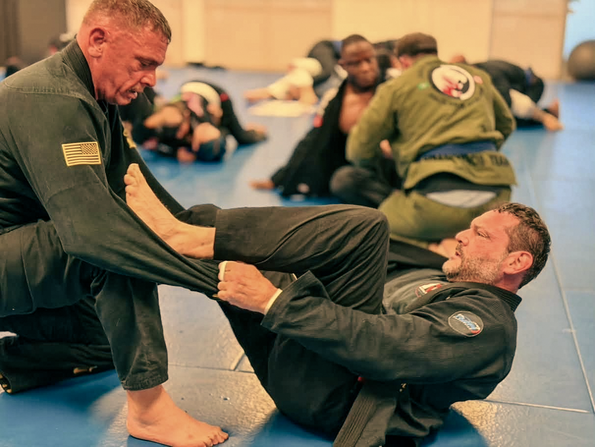 Two adults practice a ground position during a gi training round