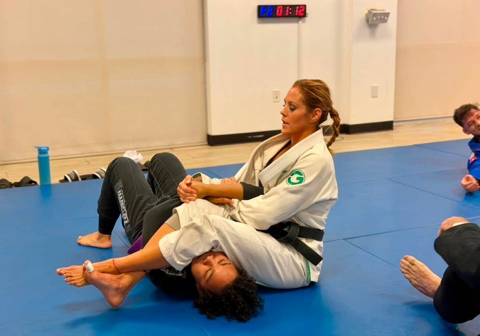A black belt in a white gi pins her training partner during a gi round