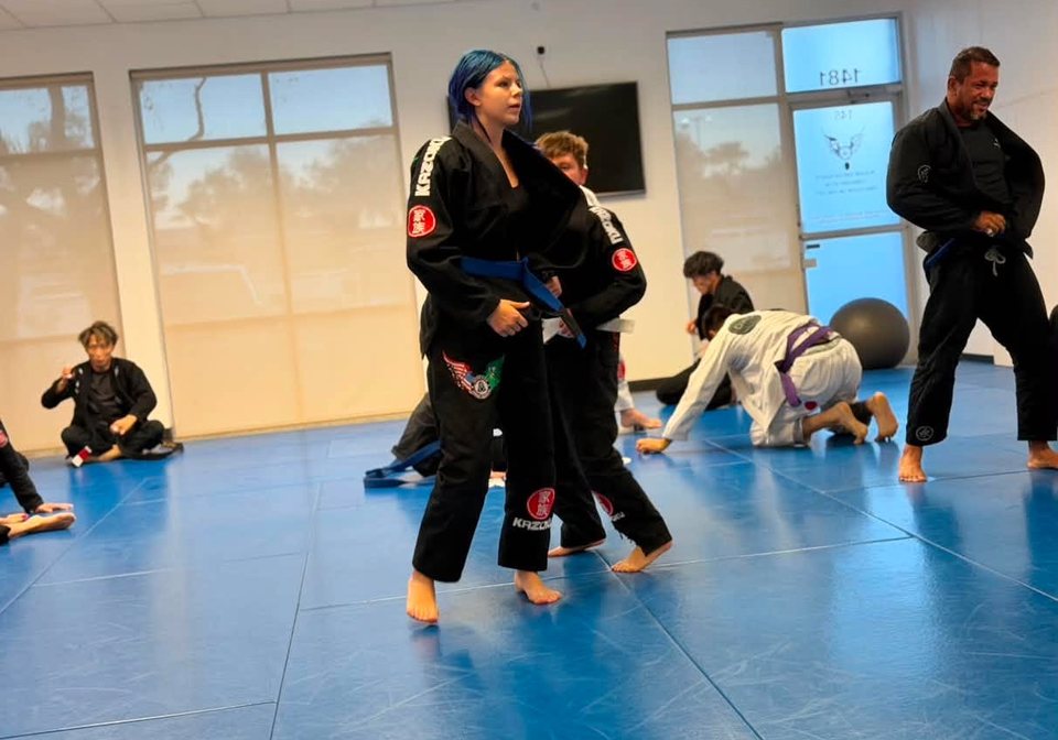 Young students in black and white gis on the Academy mat during a youth class, a coach looking on
