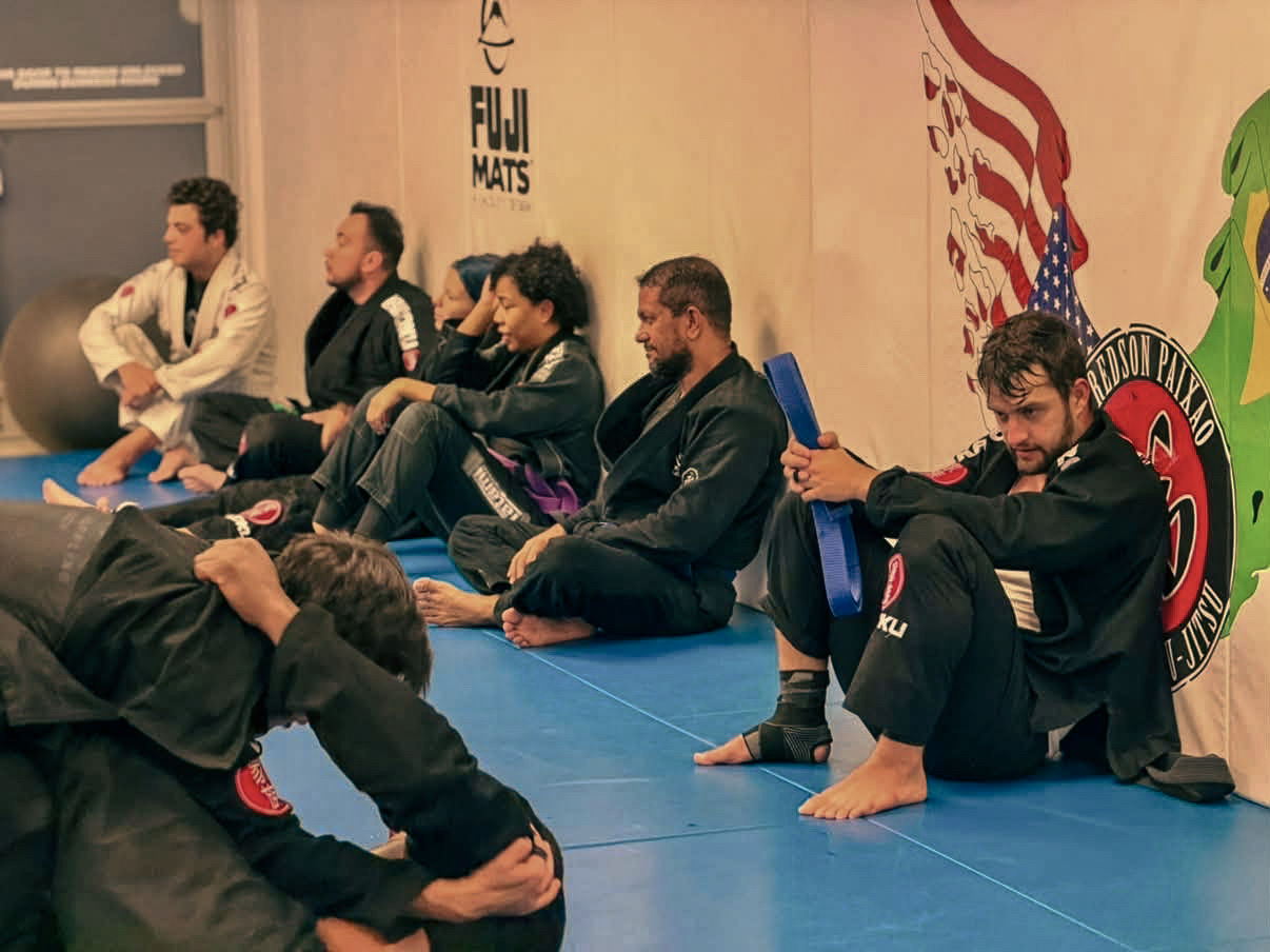 Adult practitioners seated along the side of the Academy mats between rounds